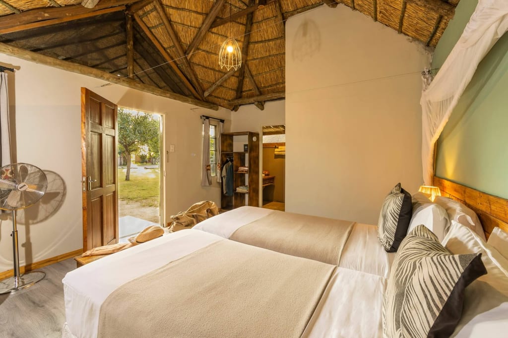 Gemütliches Schlafzimmer mit Strohdach und zwei Betten, offene Tür zum Garten und warmes Abendlicht