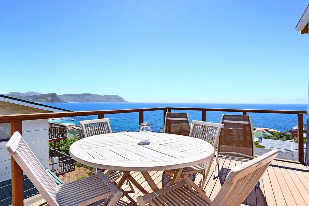 Sonnige Terrasse mit rundem Holztisch und Stühlen und weitem Meerblick unter klarem Himmel