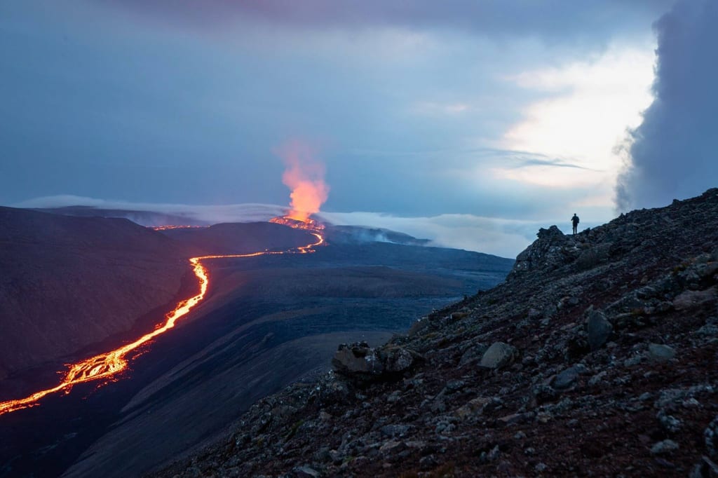 Lavafluss einer Eruption auf Reykjanes-Halbinsel mit Person als Silhouette auf Felsvorsprung.