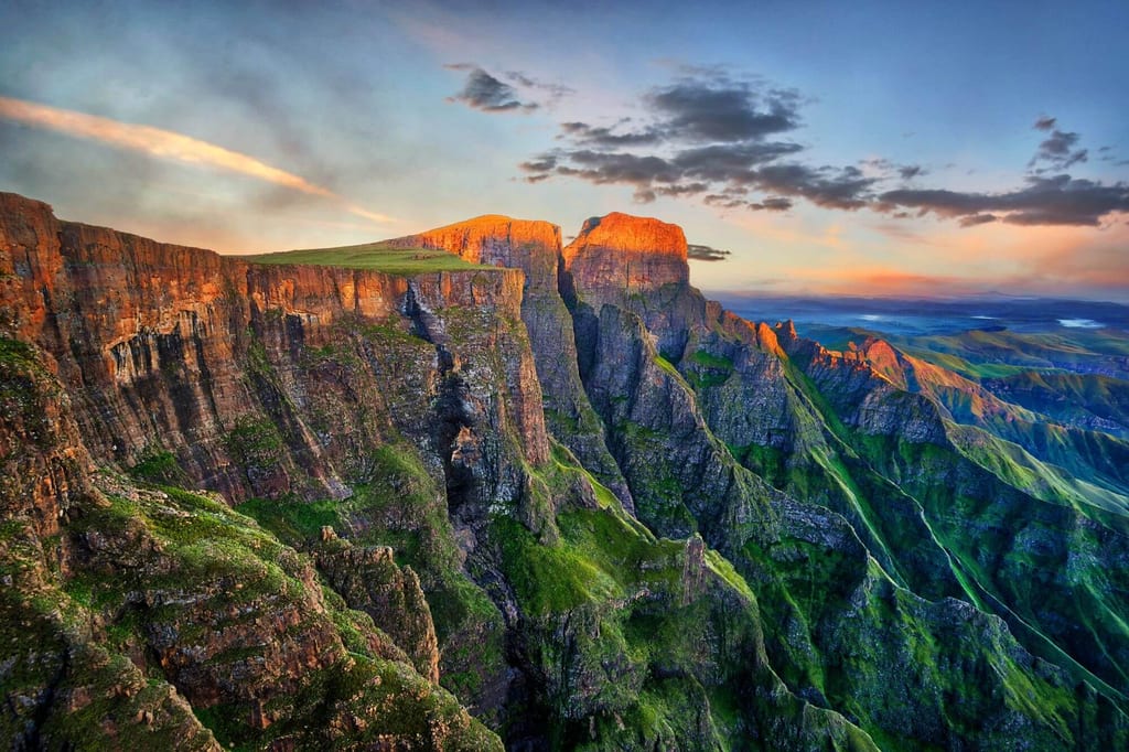 Panorama der steilen, sonnenbeschienenen Felsklippen der Drakensberge in Südafrika bei warmem Licht.