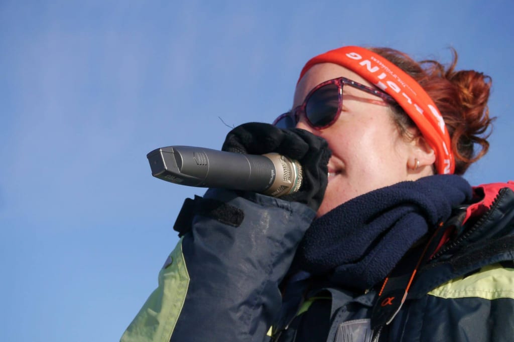 Nahaufnahme einer Person mit Mikrofon, Stirnband und Sonnenbrille vor blauem Himmel