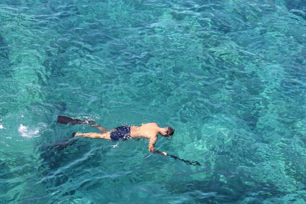 Schnorchler schwimmt mit Flossen und Maske auf klarem, türkisblauem Meer, Blick von oben.