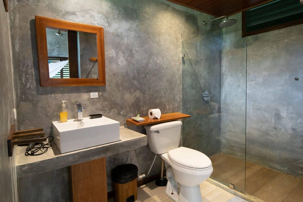 Modernes Badezimmer mit Betonwänden, Waschbecken, Toilette und Glasdusche bei Tageslicht.