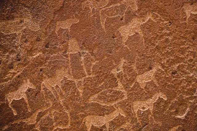 Nahaufnahme von Felsritzungen mit gravierten Tier- und menschenähnlichen Figuren auf rötlichem Gestein