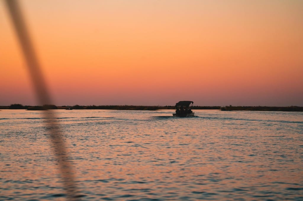 Motorboot als Silhouette auf ruhigem Wasser bei orange-rosa Sonnenuntergang, unscharfes Seil im Vordergrund.