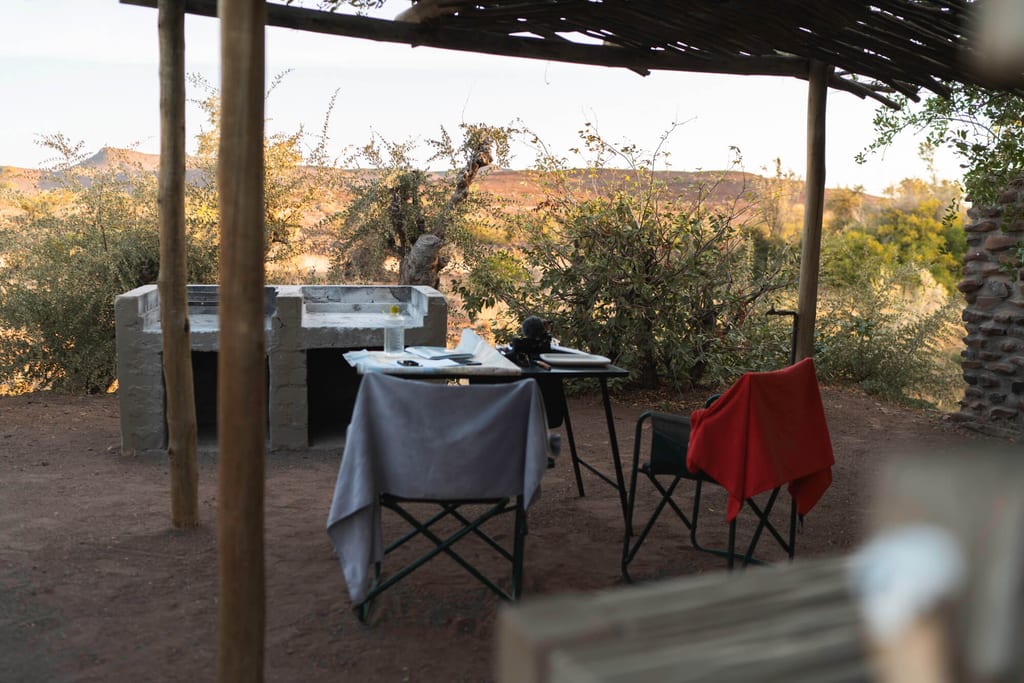 Überdachter Sitzplatz mit zwei Campingstühlen, Tisch und Blick auf sonnige Buschlandschaft