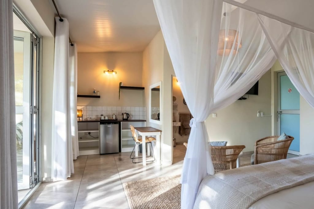 Helles Ferienzimmer mit Himmelbett, Moskitonetz, Küchenzeile und Tageslicht durch große Glasfront
