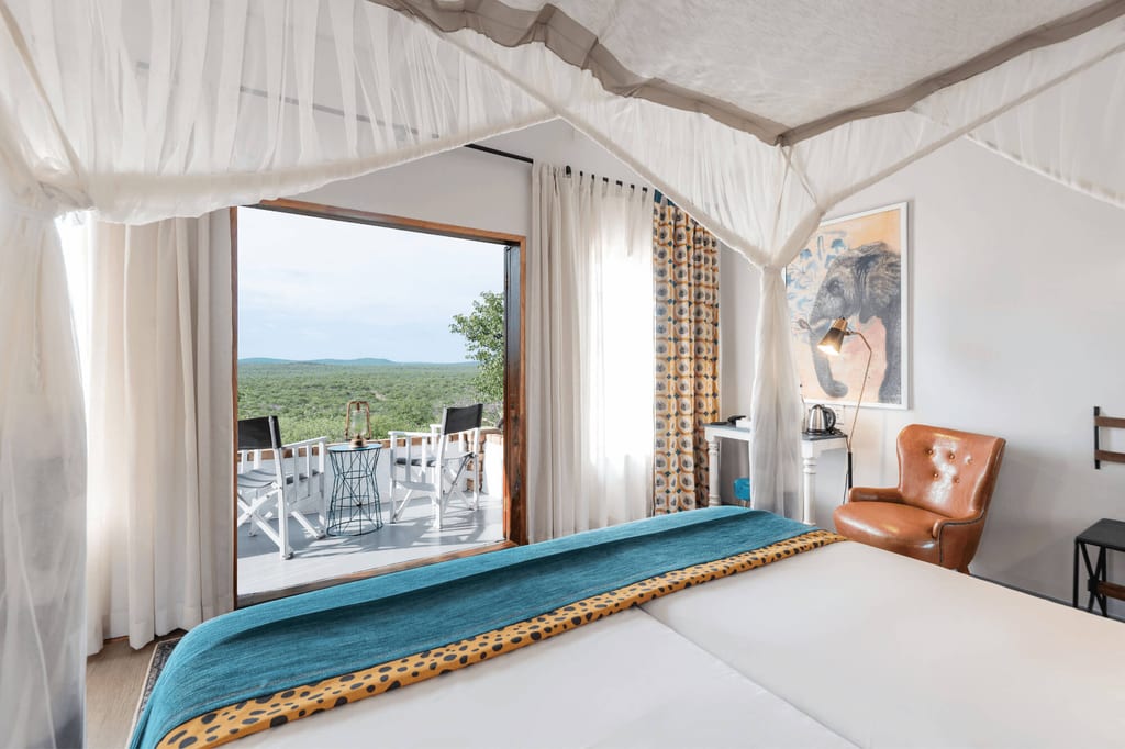 Helles Lodge-Schlafzimmer mit Moskitonetz, Balkon und weiter, bewaldeter Landschaft im Hintergrund.