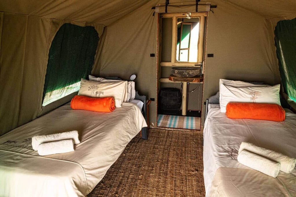 Innenansicht eines Campingzelts mit zwei Einzelbetten, orangen Handtüchern und kleinem Waschplatz