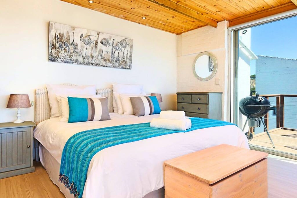 Helles Schlafzimmer mit Doppelbett, türkisem Überwurf und geöffneter Balkontür mit Grill