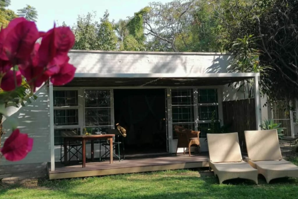 Haus mit Terrasse, zwei Liegestühlen auf Rasen und pinken Blüten im Vordergrund