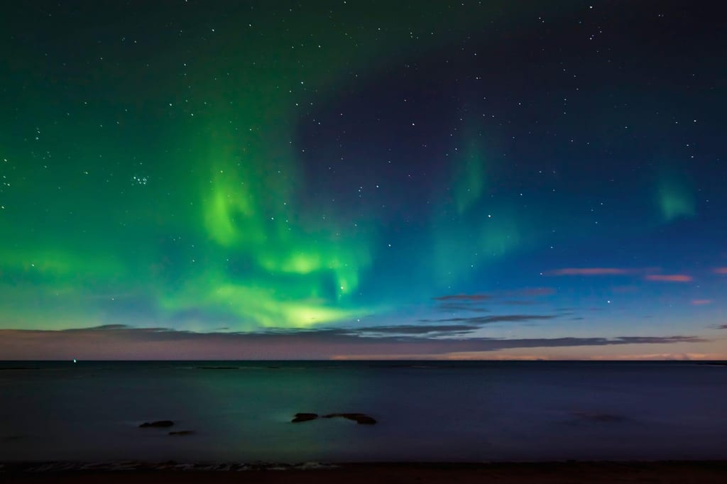 Grün leuchtendes Polarlicht über ruhiger Nachtsee am Küstenhorizont.