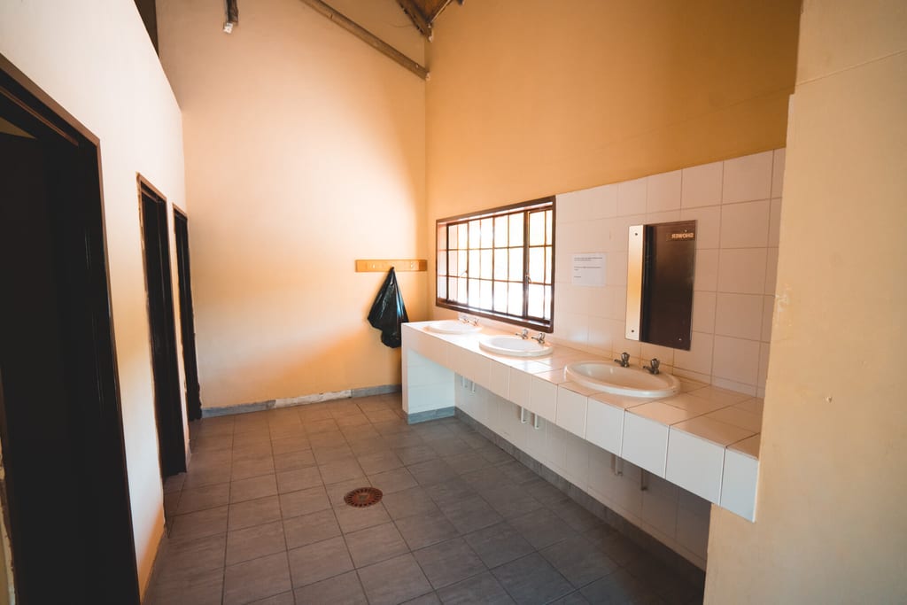 Innenraum eines einfachen Sanitärraums mit drei Waschbecken und Tageslicht durch ein Fenster.