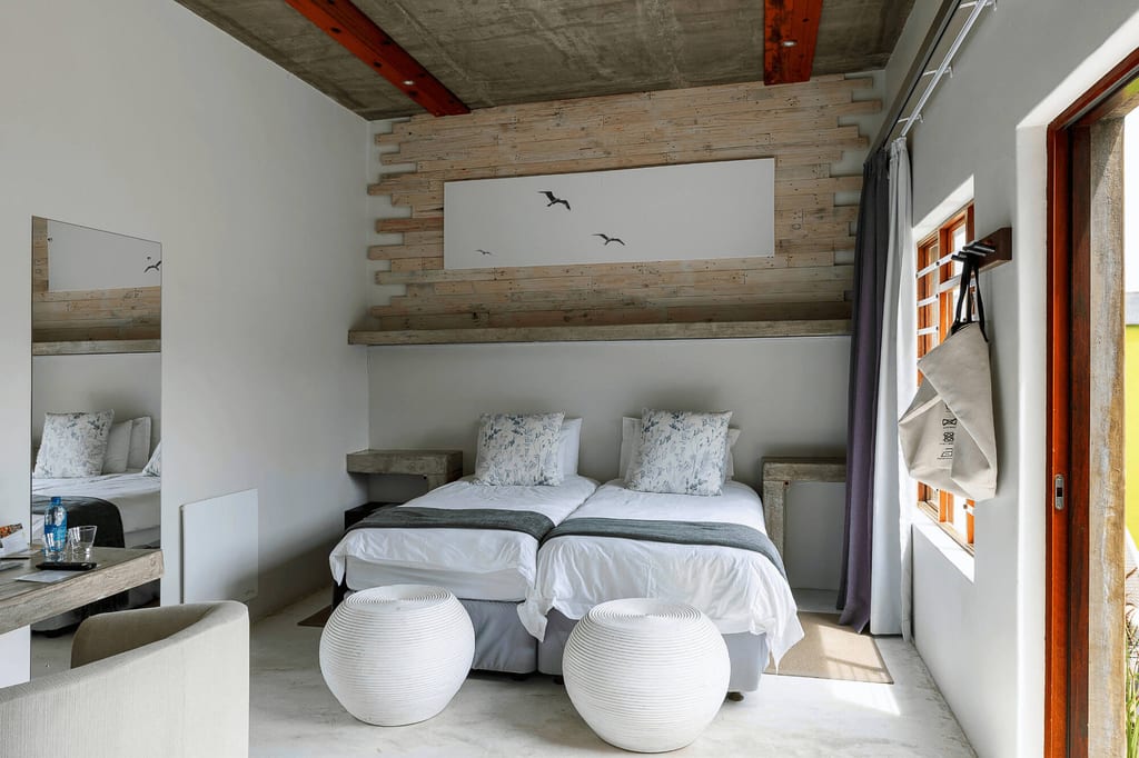 Helles Schlafzimmer mit zwei Einzelbetten, Holzverkleidung und Fenster mit Vorhang.