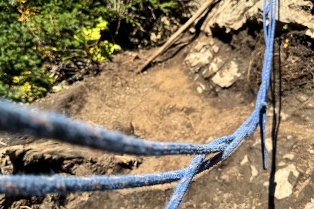 Nahaufnahme blauer Seile vor unscharfem felsigem Boden und Vegetation im Sonnenlicht.