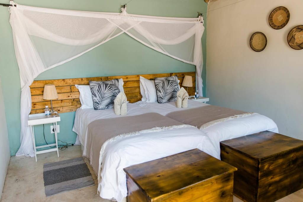 Helles Gästezimmer mit zwei einzelnen Betten, Moskitonetz und rustikalem Holzdekor.