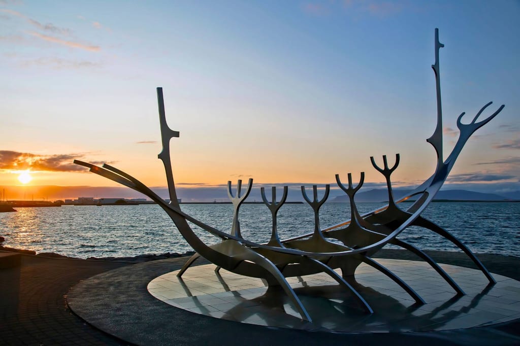 Glänzende Boots-Skulptur an der Küste bei Sonnenuntergang mit Meer und Reflexionen