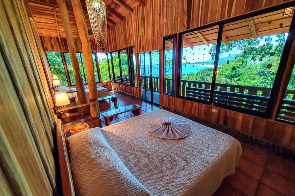 Rustikales Schlafzimmer in Holzlodge mit großen Fenstern und Blick auf Wald und Meer