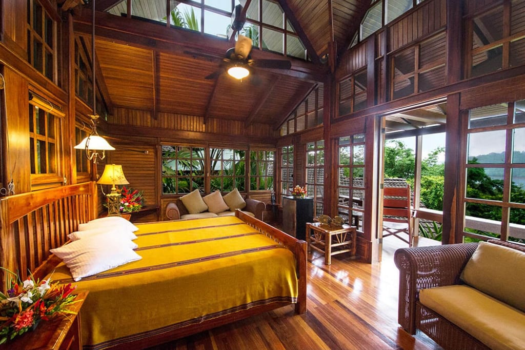 Holzschlafzimmer in Tropenbungalow mit gelber Decke und offener Veranda zum grünen Ausblick