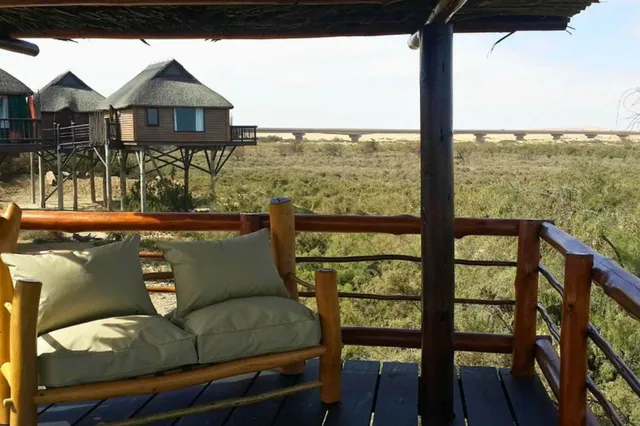 Veranda mit Holzbänkchen und Blick auf strohgedeckte Stelzenhütten und buschige Landschaft