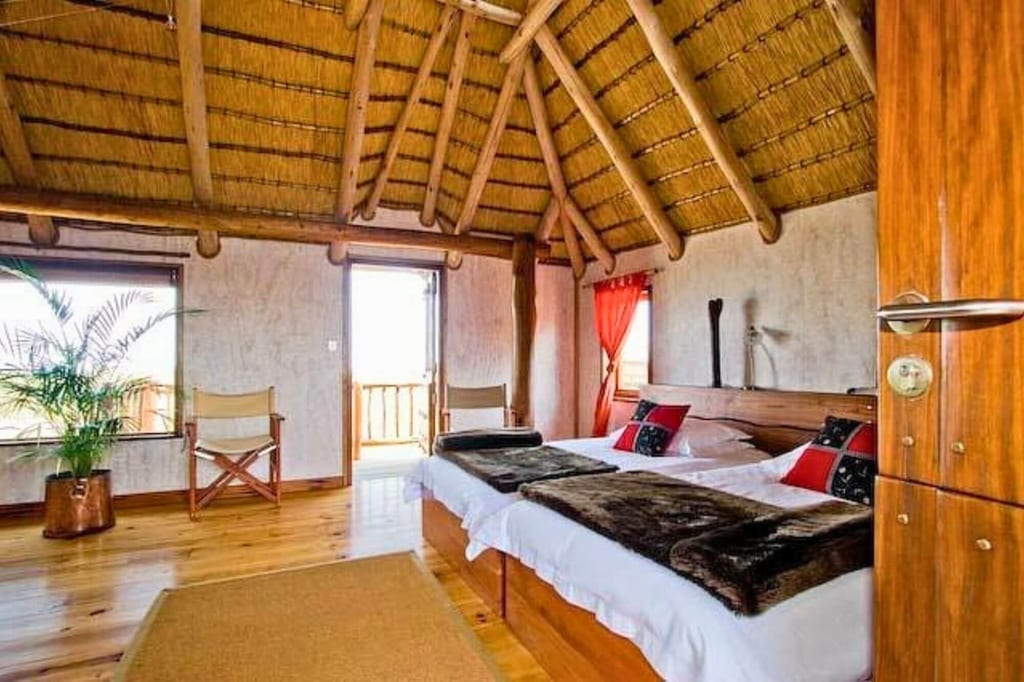 Helles Gästezimmer mit Strohdach, zwei Einzelbetten und Holzboden, Blick vom Türbereich ins Zimmer.