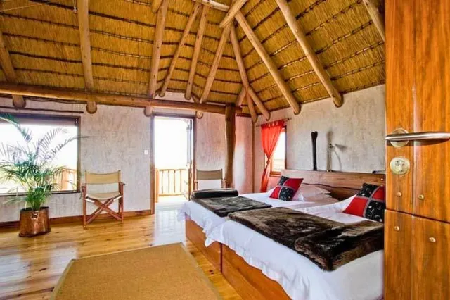 Helles Gästezimmer mit Strohdach, zwei Einzelbetten und Holzboden, Blick vom Türbereich ins Zimmer.