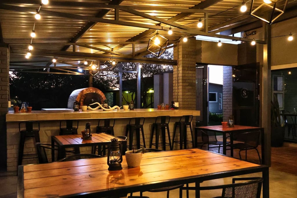 Überdachte Restaurant-Terrasse bei Dämmerung mit Holztischen und warmen Lichterketten.