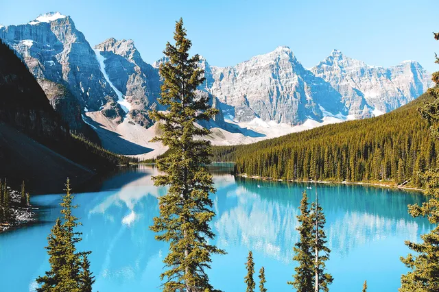 Türkisfarbener Bergsee mit Spiegelung, umgeben von Nadelwald und schroffen Gipfeln