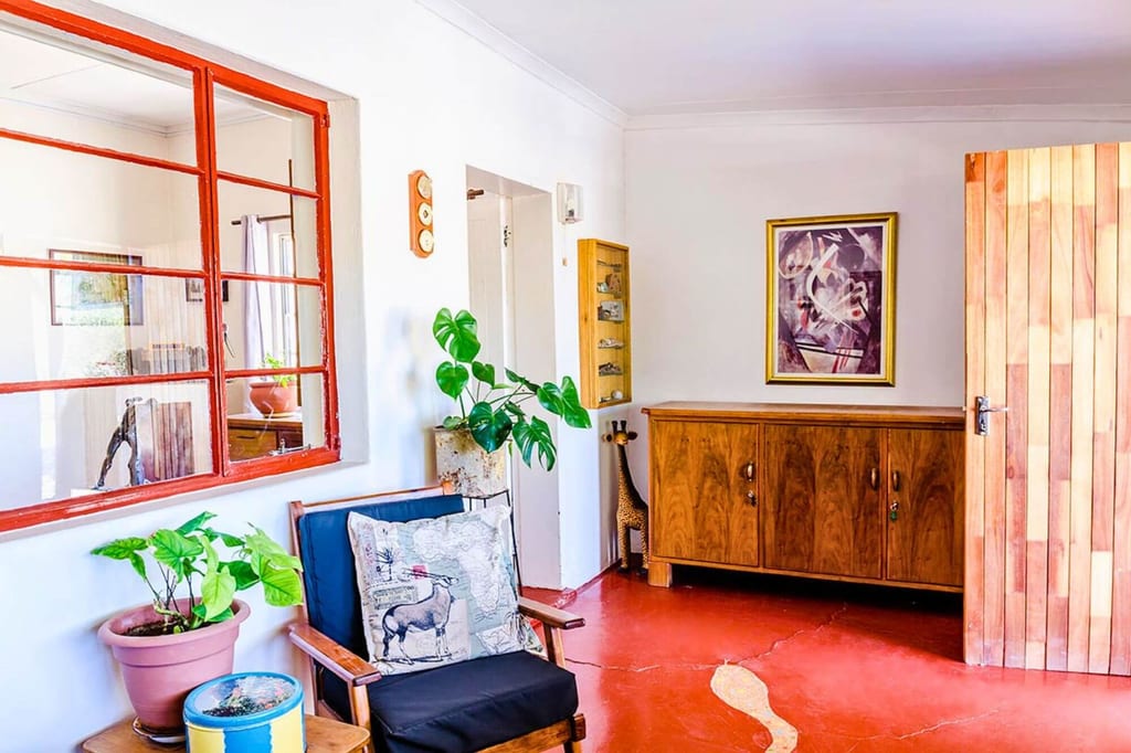 Helles Wohnzimmer mit roten Boden, Holzmöbeln, Sessel, Topfpflanzen und großem Fenster