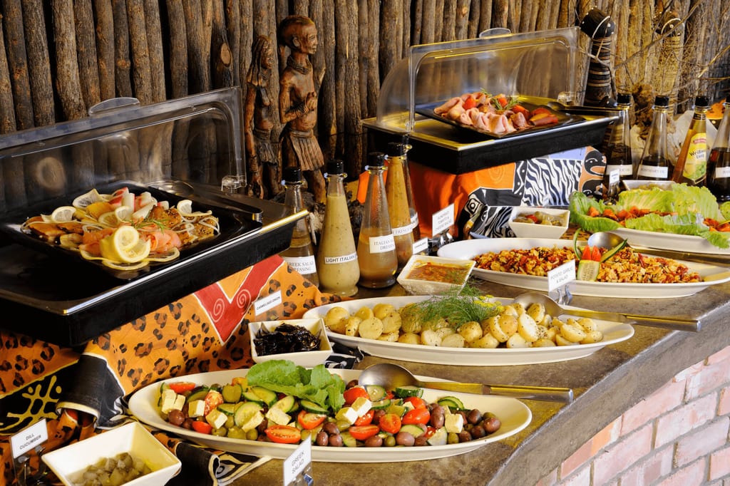Rustikales Buffet mit Salaten, Kartoffeln, Aufschnitt und Dressings vor Holzverkleidung