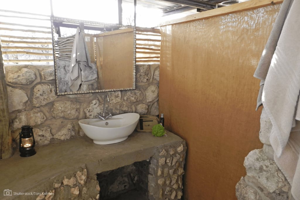 Rustikales Badezimmer mit Waschbecken, Natursteinwand, Spiegel und Handtüchern in warmem Tageslicht.