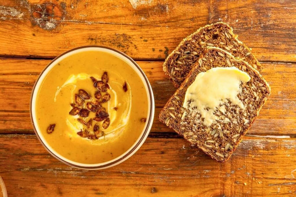Vogelperspektive: cremige Suppe mit Kernen und zwei Scheiben Mehrkornbrot auf rustikalem Holztisch.