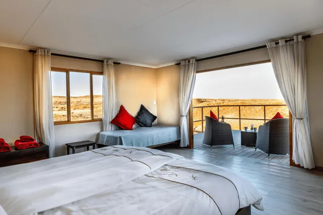 Helles Lodge-Schlafzimmer mit Doppelbett und offener Terrasse mit Sesseln und weitem, trockenem Ausblick.