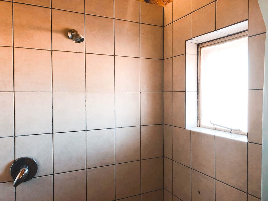 Geflieste Dusche mit Duschkopf, Einhebelmischer und Fenster, warmes Tageslicht