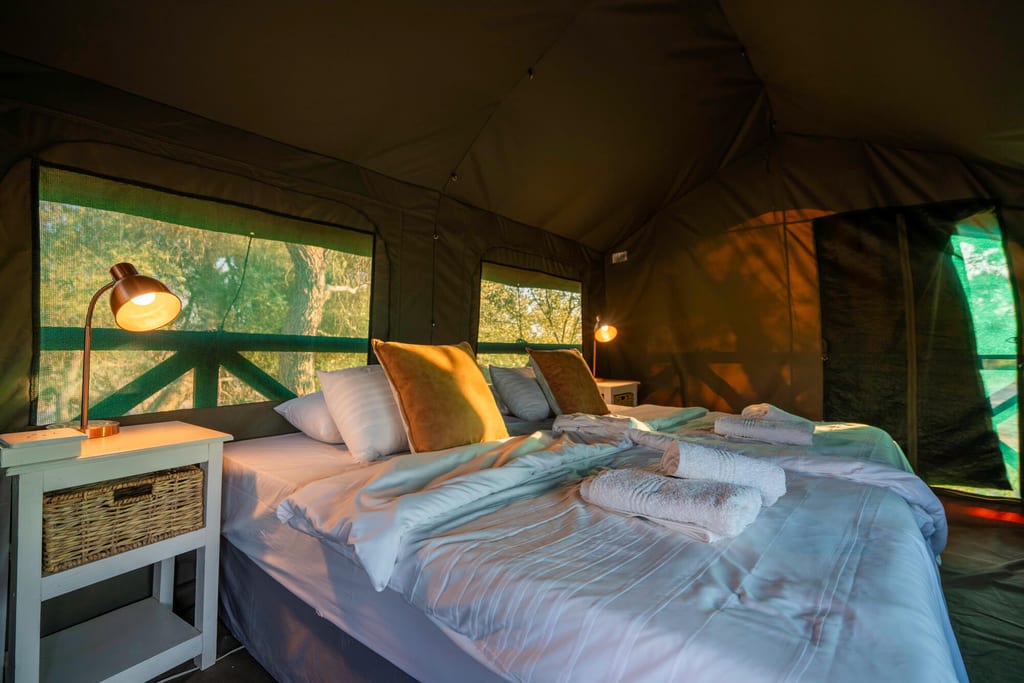Innenraum eines Glamping-Zeltes mit bezogenen Betten, warmem Licht und Blick auf einen Holzbalcon