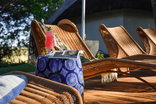 Rattanliegestühle auf Holzterrasse mit blauem Beistelltisch, Magazin und pinkem Cocktail im warmen Nachmittagslicht.