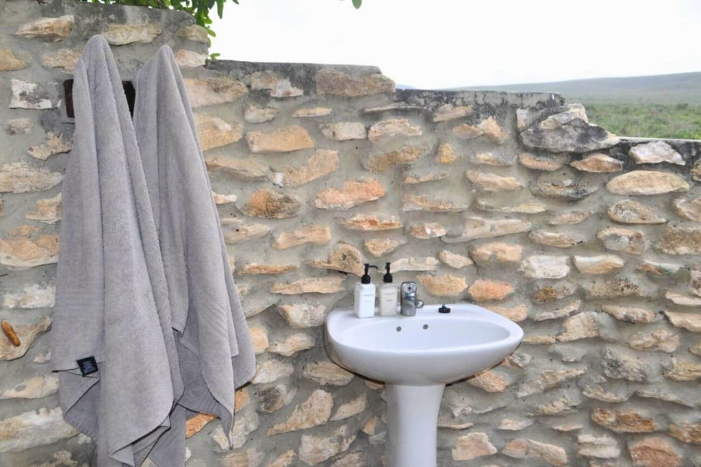 Weißes Standwaschbecken vor heller Natursteinmauer mit zwei grauen Handtüchern und Seifenspendern.