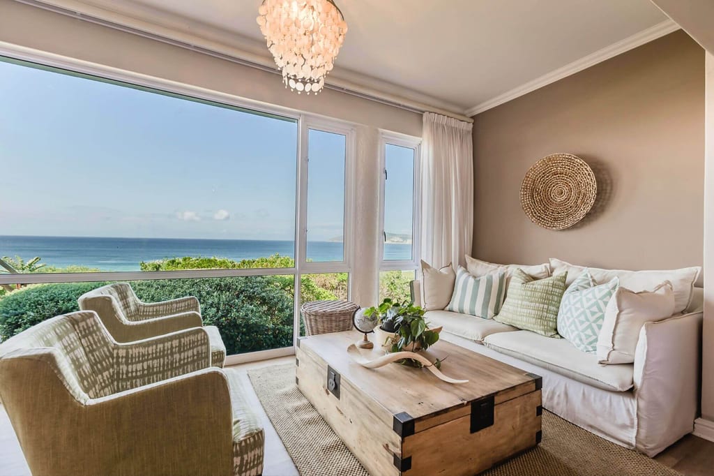 Helles Wohnzimmer mit Sofa, Sesseln und großem Fenster mit Blick auf das Meer.