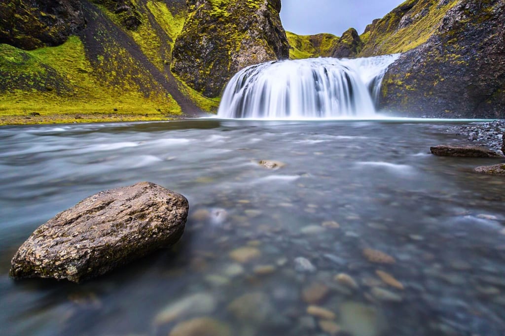 Wasserfall in moosiger Schlucht mit weichem Fluss und großem Vordergrundstein