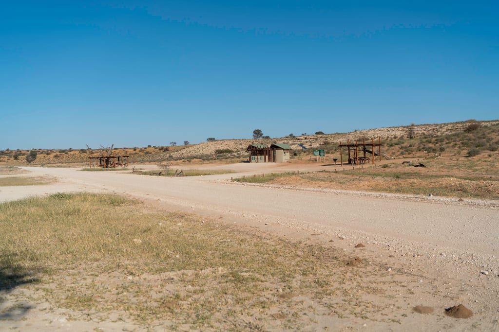 Weite Halbwüstenlandschaft mit Schotterstraße und kleinen Holzhütten unter klarem blauem Himmel