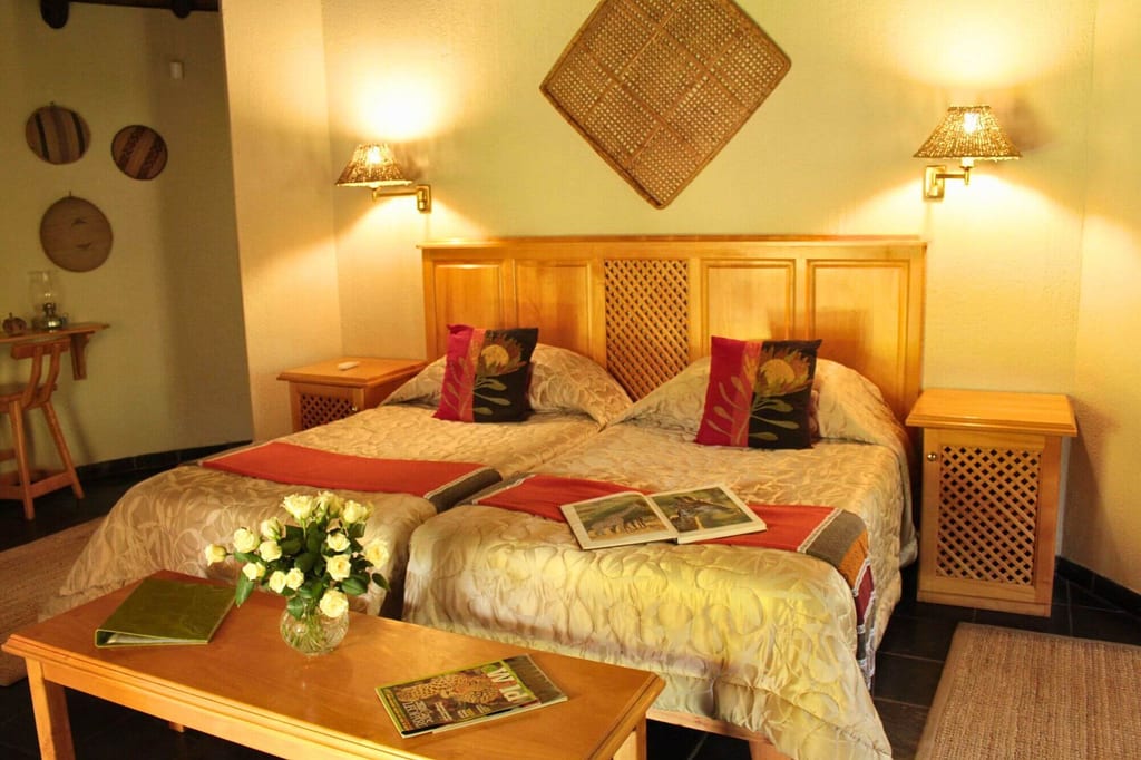Gemütliches Gästezimmer mit zwei Einzelbetten, Holzmöbeln und Vase mit weißen Rosen.