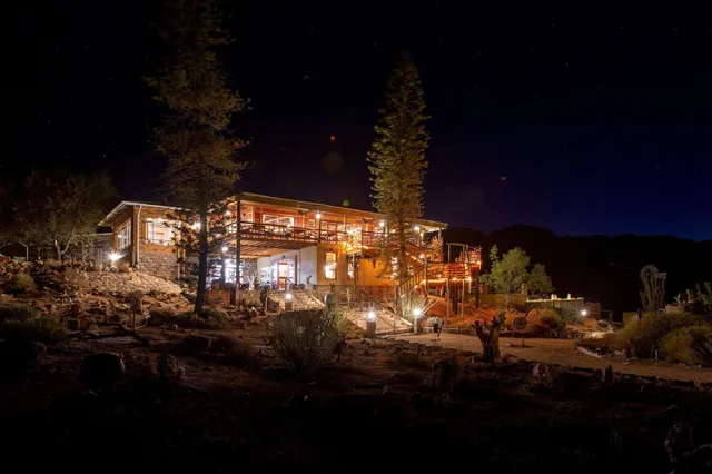 Beleuchtete Lodge bei Nacht vor klarem Sternenhimmel auf trockenem, felsigem Gelände.