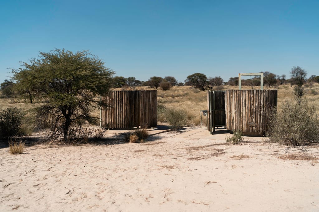 Zwei runde Holzkabinen auf sandigem Boden in trockener Savannenlandschaft bei klarem Himmel