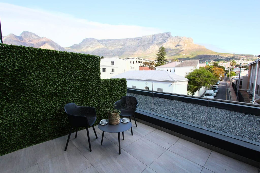 Dachterrasse mit zwei Stühlen, kleinem Tisch und Blick auf Häuser und markanten Bergkamm im Hintergrund.