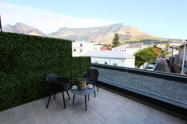 Dachterrasse mit zwei Stühlen, kleinem Tisch und Blick auf Häuser und markanten Bergkamm im Hintergrund.