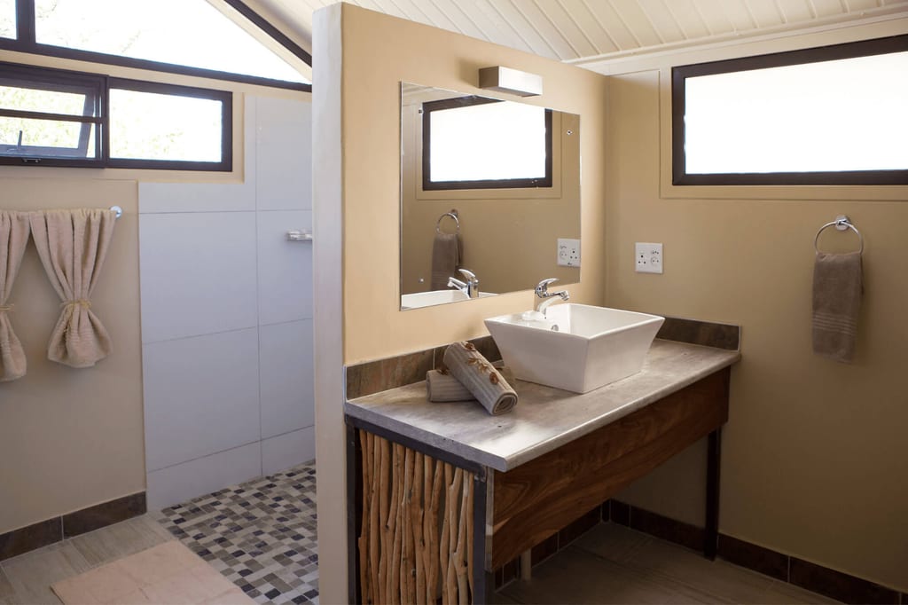 Modernes Badezimmer mit Waschbecken, Spiegel und offener Dusche bei Tageslicht.