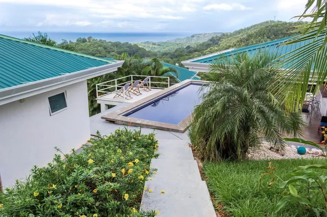 Terrassenblick mit Pool, Palmen, gelben Blumen und Meerblick unter bewölktem Himmel