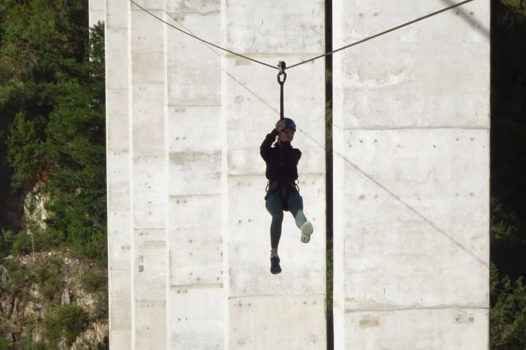 Person in Klettergurt auf Zipline zwischen Betonpfeilern bei Tageslicht