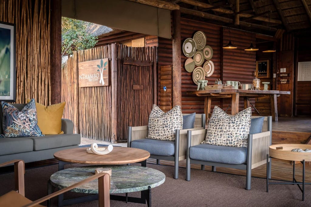 Rustikale Lodge-Lounge mit Sofa, Sesseln und Holzwänden in warmem Tageslicht, gemütliche Einrichtung.