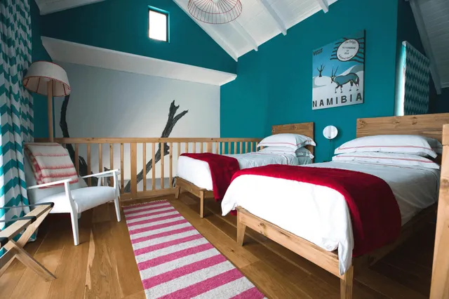 Gästezimmer mit zwei Einzelbetten, türkisen Wänden und roter Bettdecke, heller Holzboden